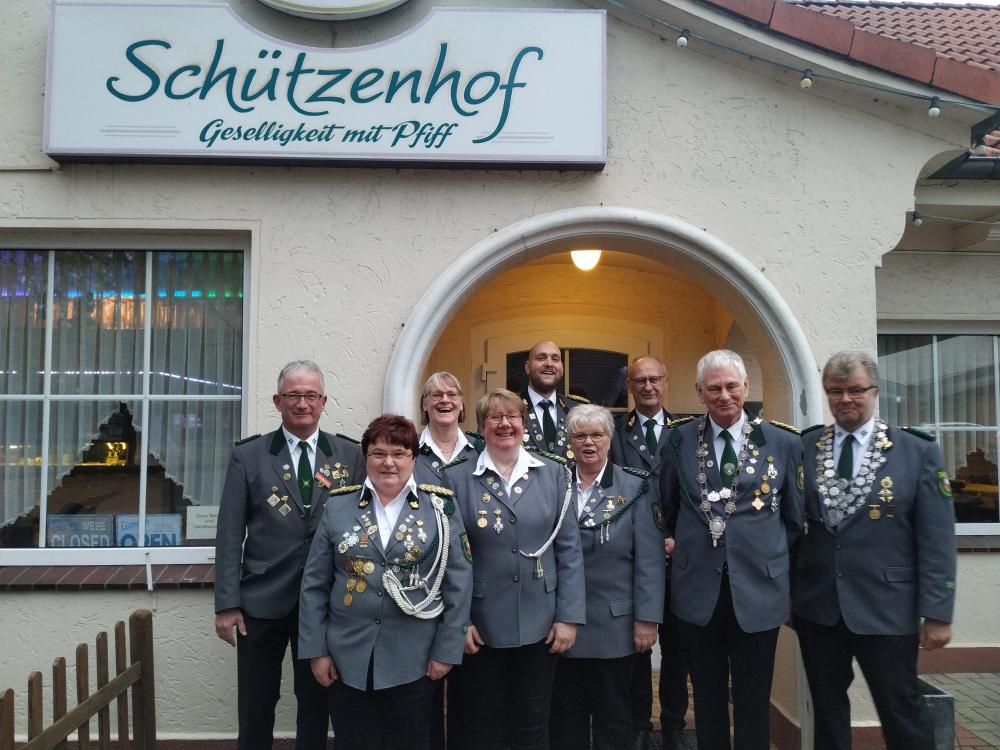 Die Mitglieder des aktuellen Vorstand und Beirates des SV Ganderkesee stehen in Uniform vor dem Eingang des Schützenhofs. Das Logo des Schützenhof ist über ihren Köpfen an der Wand angebracht. Der Vorstand lacht.