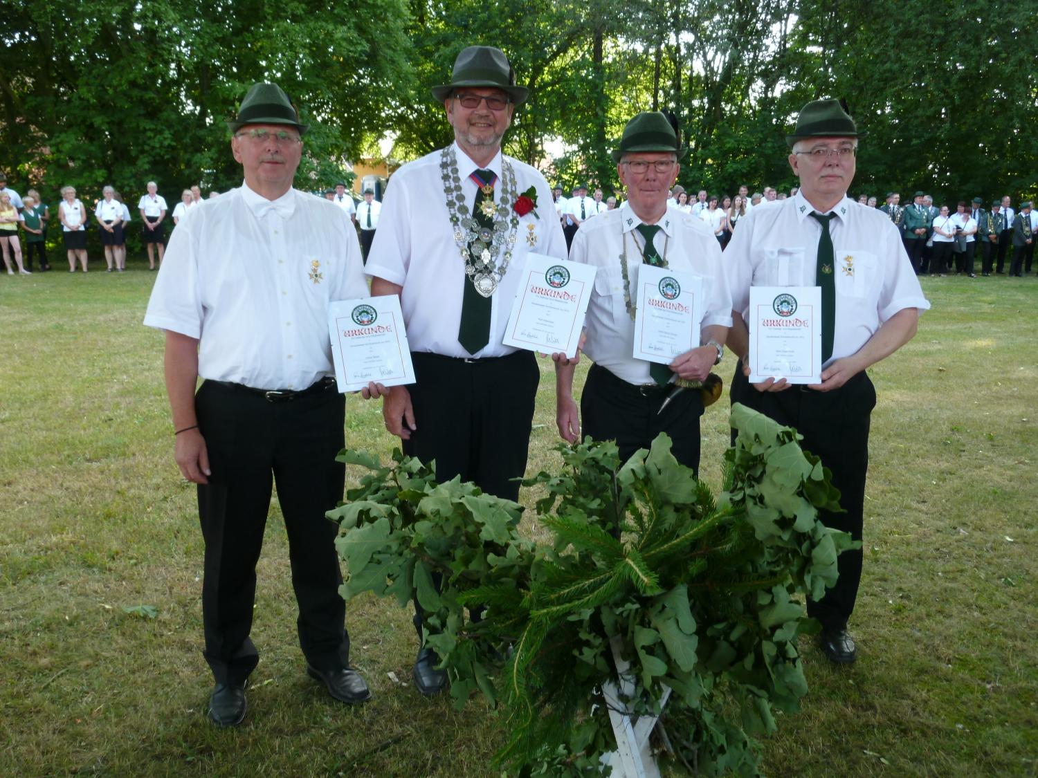 Lothar Meyer, Ralf Hüttemeyer, Heinz-Georg Tönnies, Hans-Jürgen Holte stehen vor den versammelten Schützen und halten ihre Urkunden für langjährige Mitgliedschaft in den Händen.