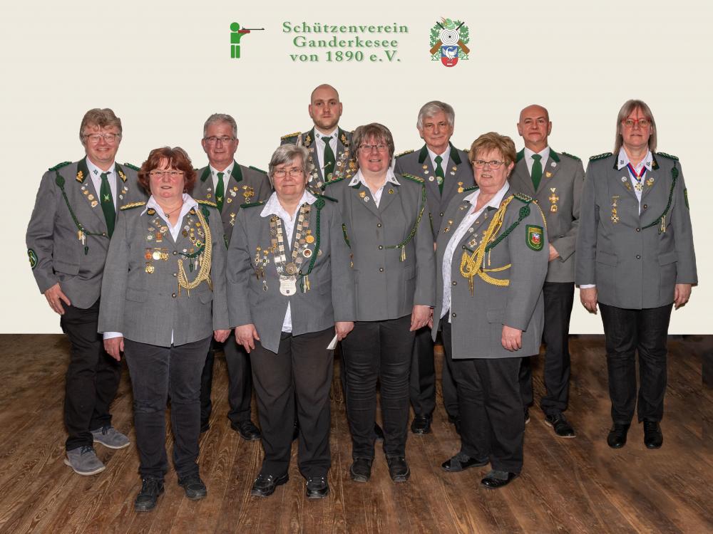 Die Mitglieder des aktuellen Vorstand und Beirates des SV Ganderkesee stehen in zwei Reihen in Uniform vor einer weißen Wand. Das Logo des SV Ganderkesee ist über ihren Köpfen abgebildet.